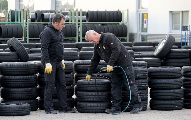 Två män arbetar med att testa däck. De står framför en välorganiserad hög av nya däck.