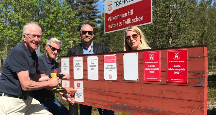 Kjell Jonsson från M Sveriges lokalklubb monterar upp skylten "Länets bästa rastplats 2019" omgiven av representanter från Trafikverket samt skötselansvarig.